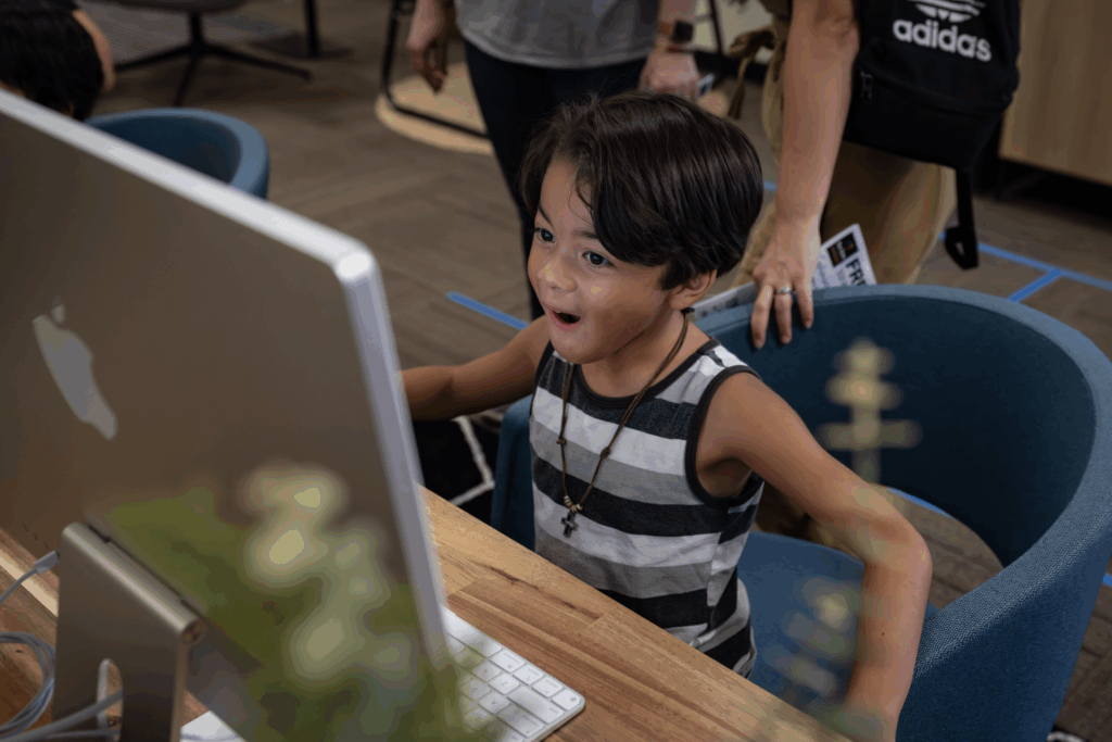 A little kid sits at a computer screen marveling at what he is making
